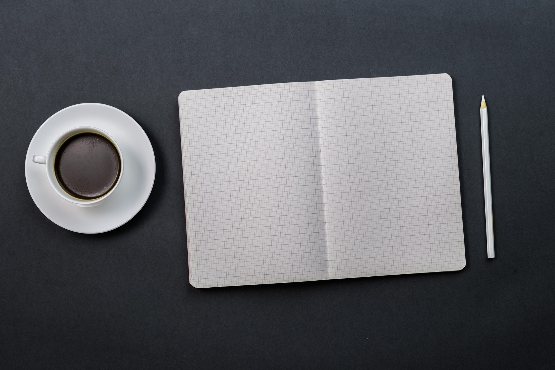 Black coffee and an open notebook with a white pencil on a black table